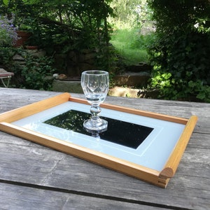Könnte beinhalten: Ein Holztablett mit einem hellblauen und weißen Rahmen und einem schwarzen Spiegel im Inneren. Ein klares Glas steht auf dem Spiegel.