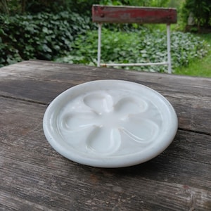 Könnte beinhalten: Weiße Keramik-Schale mit einem blütenförmigen Design. Die Schale hat fünf abgerundete Vertiefungen in der Mitte.