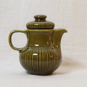 Könnte beinhalten: Eine grüne Keramik-Milchkanne mit Deckel. Die Kanne hat ein geripptes Design und einen runden Körper.