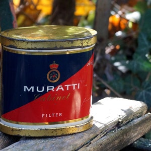Könnte beinhalten: Eine Vintage-Blechdose für Muratti Cabinet Filter Zigaretten. Die Dose ist blau, rot und goldfarben mit einer Krone und dem Aufdruck "Muratti Cabinet Filter".