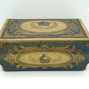 Könnte beinhalten: Eine antike blaue und goldene Blechdose mit einem dekorativen Design und dem Text "A.C. Streitburg" auf der Vorderseite.