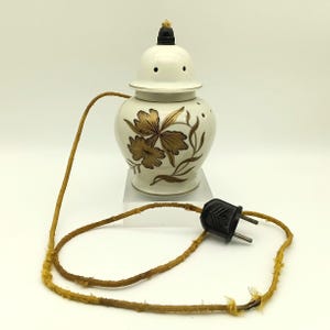 Könnte beinhalten: Weißer elektrischer Ölbrenner aus Keramik mit goldenem Blumendesign und schwarzem Stromkabel.