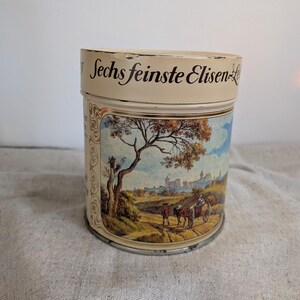 Könnte beinhalten: Vintage zylindrische Dose mit cremefarbenem Deckel und Boden. Der Korpus zeigt eine Landschaftsszene mit einem Baum, Figuren und einer Stadt. Der Text "Sechs feinste Elisen-" ist in schwarzer Schrift auf dem Deckel aufgedruckt.