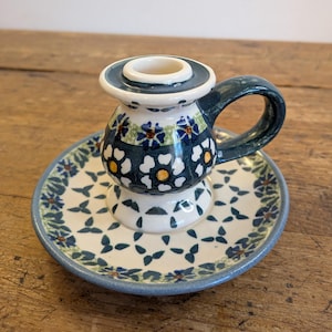 Könnte beinhalten: Ein Kerzenhalter aus Keramik mit Griff, mit weißem Sockel und dunkelblauem Blumenmuster. Der Halter steht auf einer passenden Untertasse mit blauem Rand und Blumendesign. Der Kerzenhalter ist ein dekorativer Artikel.