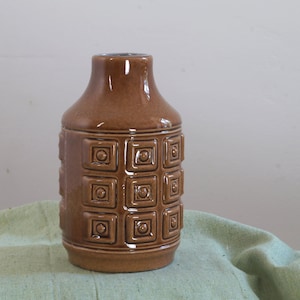 Könnte beinhalten: Eine braune Keramikvase mit geometrischem Muster. Die Vase hat ein quadratisches Design mit erhabenen Kreisen in jedem Quadrat.