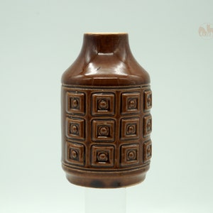 Könnte beinhalten: Eine braune Keramikvase mit einem geometrischen Muster aus Quadraten und Kreisen. Die Vase hat einen runden Körper und einen schmalen Hals.