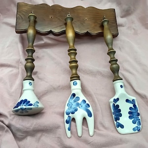 Könnte beinhalten: Drei Keramik-Küchenutensilien mit blauen und weißen Blumenmustern hängen an einem Holzgestell. Die Utensilien umfassen einen Servierlöffel, eine Gabel und eine Schöpfkelle.