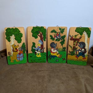 Könnte beinhalten: Vier Wandtafeln aus Holz mit bemalten Zeichentrickfiguren und Szenen. Zu den Figuren gehören ein gelber Hund, Donald Duck, ein Igel und Vögel. Jede Tafel hat einen grünen Baum und einen Holzrahmen.