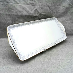 Könnte beinhalten: Ein rechteckiges Serviertablett in Weiß mit goldfarbenem Rand und einem grauen und weißen geometrischen Muster am Rand.