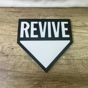 Peut inclure: Une pancarte de décoration intérieure noire et blanche avec le mot "REVIVE" en lettres blanches sur fond noir. La pancarte est en forme de losange et a un intérieur blanc.