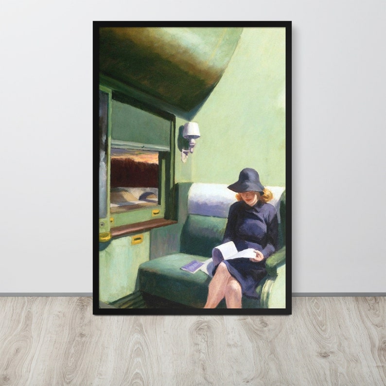 May include: A woman in a black hat and dress sits on a green train seat reading a book. The train window is visible behind her, showing a view of a landscape.