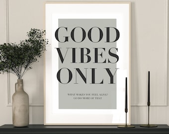 May include: A black and white framed print with the text "GOOD VIBES ONLY" and the smaller text "WHAT MAKES YOU FEEL ALIVE? GO DO MORE OF THAT". The print is hanging above a black fireplace mantel with a black fireplace and two black chairs. The fireplace mantel is decorated with two black candle holders with gold accents.