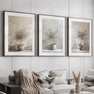 May include: A living room interior featuring a sectional sofa, three framed botanical prints, a coffee table, two side tables, and two ottomans. The sofa is upholstered in a light beige fabric and has a throw blanket draped over it. The coffee table is made of wood and has a glass top. The side tables are made of wood and have a black finish. The ottomans are upholstered in a light grey fabric.