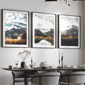 May include: A contemporary dining room featuring a dark wood table, grey chairs, and three framed landscape prints. A black and silver chandelier hangs above the table. The room has a neutral colour palette with natural light.