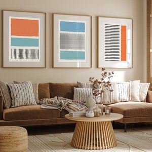 Könnte beinhalten: Ein braunes Ecksofa mit einer Wolldecke und Kissen in einem Wohnzimmer mit drei abstrakten Kunstdrucken an der Wand. Die Drucke zeigen geometrische Formen in Orange, Blau und Schwarz.