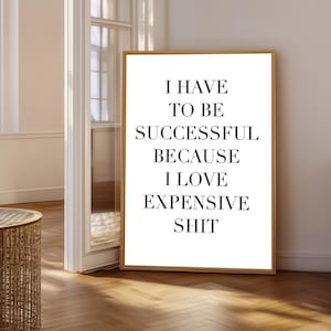 Könnte beinhalten: Ein rechteckiges Wandbild in einem dünnen Holzrahmen mit schwarzem Text auf weißem Hintergrund, der lautet: I HAVE TO BE SUCCESSFUL BECAUSE I LOVE EXPENSIVE SHIT. Die Typografie ist klar, fett gedruckt und innerhalb des Rahmens zentriert.