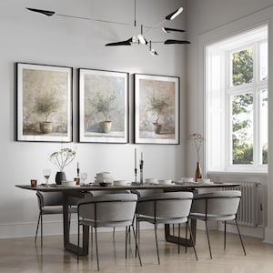 May include: A dining room with a wooden table and six gray chairs. Three framed prints of olive trees in pots hang on the wall. A black modern light fixture hangs above the table.