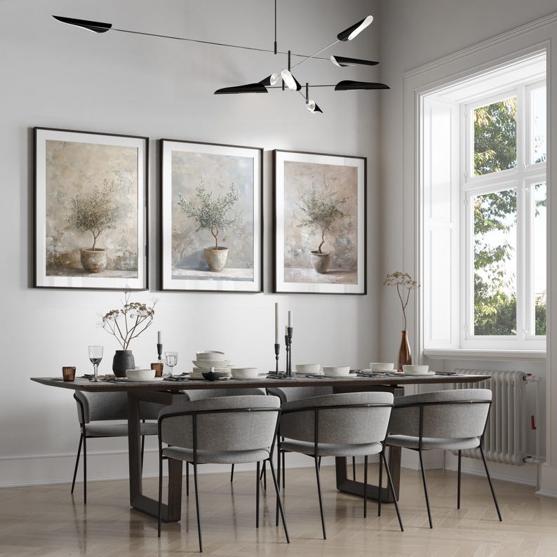 May include: A dining room with a wooden table and six gray chairs. Three framed prints of olive trees in pots hang on the wall. A black modern light fixture hangs above the table.