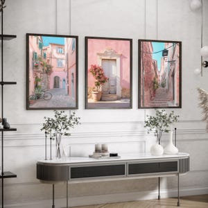 May include: Three framed prints of colorful, narrow streets in a European city. The prints are hung on a white wall above a gray console table.