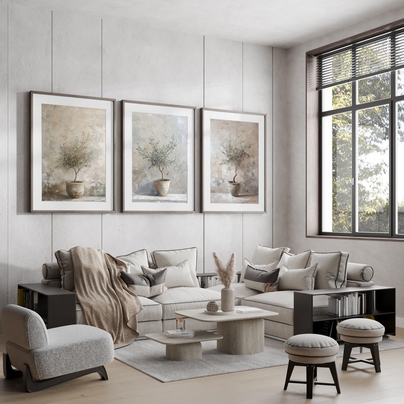 May include: A living room interior with a sectional sofa, three framed botanical prints, a coffee table, two side tables, and two ottomans. The sofa is covered in a light beige fabric and has a throw blanket draped over it. The coffee table is made of wood and has a glass top. The side tables are made of wood and have a black finish. The ottomans are covered in a light gray fabric.
