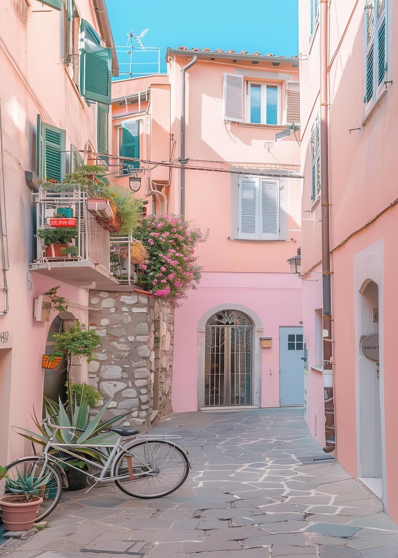 May include: A narrow, cobblestone alleyway in a European city with pink buildings and a bicycle parked on the side. The buildings have white shutters and a wrought iron gate.
