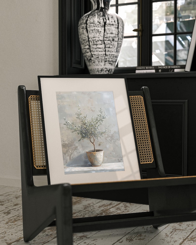 May include: A framed print of a watercolor painting of a small olive tree in a terracotta pot. The tree is green and the background is a soft blue and gray.