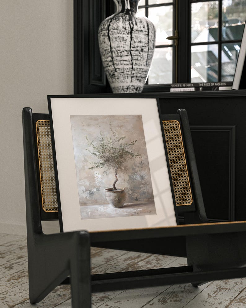 May include: A framed print of a watercolor painting of a small olive tree in a terracotta pot. The tree is in a light brown pot and is set against a light brown background with hints of green and blue.