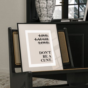 May include: A black framed print with a beige background and black text that reads "LIVE. LAUGH. LOVE. DON'T BE A CUNT."