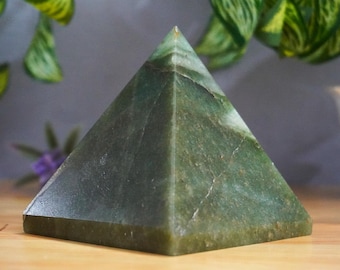 May include: A green gemstone pyramid with a smooth, polished surface. The pyramid is made of natural stone and has a light green color with darker green veins.