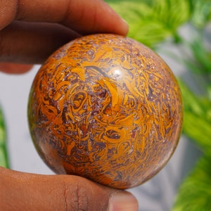 May include: A polished, spherical, brown and gold stone with intricate swirling patterns. The stone is smooth and has a glossy finish.