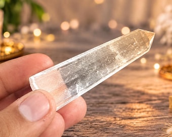 May include: A clear, faceted quartz crystal point with a hexagonal shape and a pointed tip. The crystal is transparent with visible internal inclusions and a smooth, polished surface, reflecting light across its elongated, geometric structure.