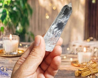 May include: A clear, faceted quartz crystal point with visible internal inclusions and fractures, featuring a hexagonal shape that tapers to a point at the top, held upright to display its translucent and reflective crystalline structure.
