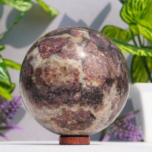 Pode incluir: Uma esfera polida de lepidolita rosa e cinza com um padrão de redemoinho. A esfera está em um suporte de madeira.