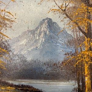 May include: Oil painting of a mountain landscape. A snow-capped mountain dominates the background, with a lake and trees in the foreground. The trees have yellow leaves, suggesting autumn. The painting has a textured, impressionistic style.
