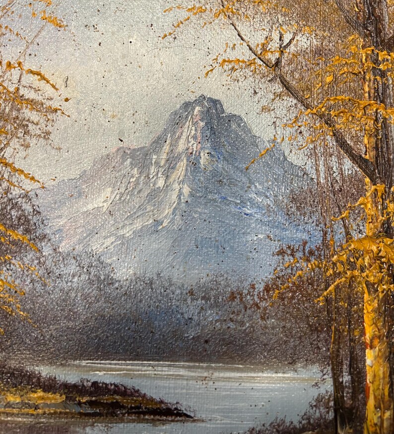 May include: Oil painting of a mountain landscape. A snow-capped mountain dominates the background, with a lake and trees in the foreground. The trees have yellow leaves, suggesting autumn. The painting has a textured, impressionistic style.