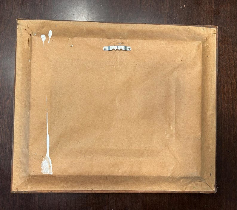 May include: Back of a framed artwork. The frame is brown, and the backing is a light brown paper. A metal sawtooth hanger is attached to the top center. White paint splatters are visible on the backing.