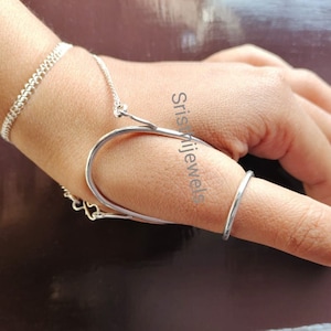 以下が含まれることがあります： ユニークなデザインのシルバーの親指リング。リングは2つの部分で構成されており、1つは親指に巻き付け、もう1つは親指の上を通る。リングは存在感のあるアイテムで、個性を演出したい人におすすめです。