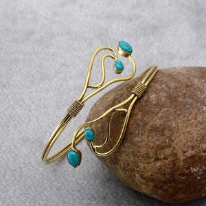 Könnte beinhalten: Ein goldfarbenes Armreif-Armband mit einem zarten, organischen Design, das mit türkisfarbenen Edelsteinen besetzt ist. Das Armband ist offen und verstellbar.