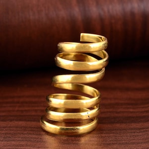 Könnte beinhalten: Ein goldfarbener Spiralring mit fünf Bändern. Der Ring ist aus Metall und hat eine glatte, polierte Oberfläche.