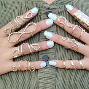 May include: A set of gold-toned rings with various designs, including a snake, a wave, and an infinity symbol. The rings are worn on multiple fingers.