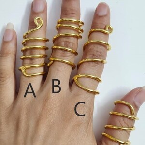 May include: Four gold spiral rings on a hand. The rings are labeled A, B, C, and D.