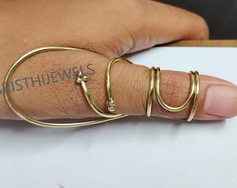 May include: A gold thumb ring with a decorative design. The ring is made of multiple bands of metal that wrap around the thumb. The ring is worn on a person's thumb.