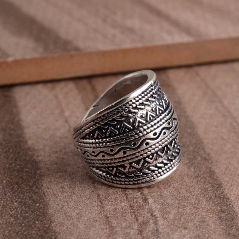 Peut inclure: Une bague en argent avec une large bande orn&eacute;e d'un motif g&eacute;om&eacute;trique complexe. Le motif est compos&eacute; de triangles, de lignes et de points r&eacute;p&eacute;t&eacute;s.