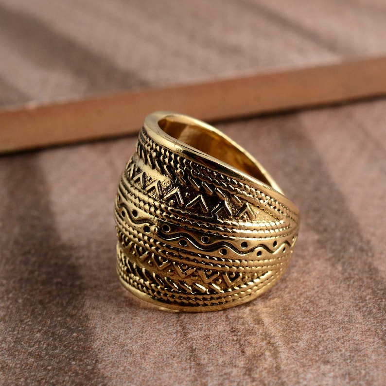 Peut inclure: Une bague en m&eacute;tal de couleur or avec une large bande orn&eacute;e d'un motif g&eacute;om&eacute;trique complexe. La bague est lisse et polie.