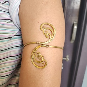 May include: A gold-toned arm cuff with a decorative design of swirling lines and dots.