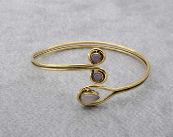 May include: A gold-toned bangle bracelet with a double-loop design and three purple and pink stones.