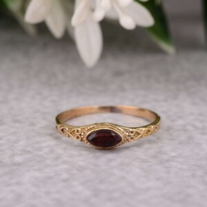 Könnte beinhalten: Ein goldener Ring mit einem roten Edelstein, der in einem filigranen, verzierten Design gefasst ist.
