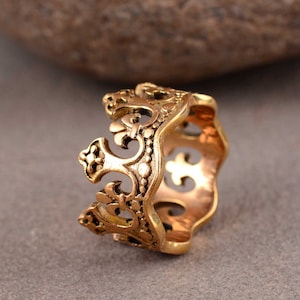 Puede incluir: Un anillo de tono dorado con un diseño de corona. El anillo está intrincadamente detallado con un patrón de filigrana.