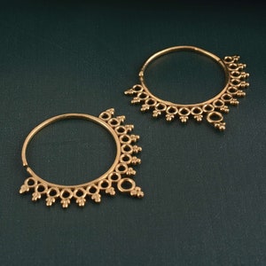 Könnte beinhalten: Zwei goldene Creolen mit einem dekorativen Design. Die Ohrringe haben eine kreisförmige Form mit einem detaillierten Muster aus kleinen Kreisen und Punkten am Rand.