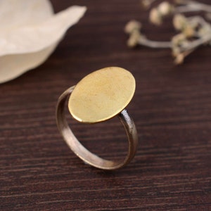 Könnte beinhalten: Ein goldener Ovalring mit einer glatten, flachen Oberseite. Der Ring ist aus Messing und hat ein schlichtes, minimalistisches Design.